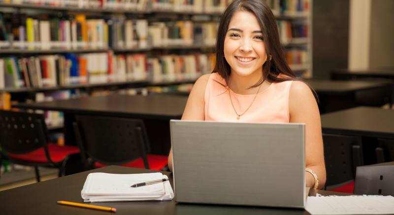 Muchacha estudiando pedagogía en línea en biblioteca