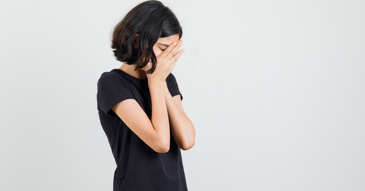 little-girl-clasping-hands-face-black-t-shirt-looking-sad-front-view